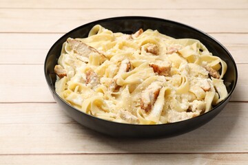 Tasty Alfredo pasta with chicken on light wooden table