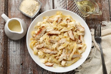 Tasty Alfredo pasta with chicken served on wooden table, flat lay