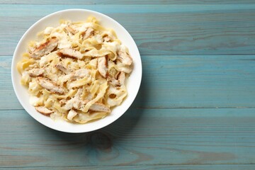 Tasty Alfredo pasta with chicken on light blue wooden table, top view. Space for text