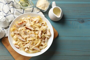 Tasty Alfredo pasta with chicken on light blue wooden table, flat lay. Space for text