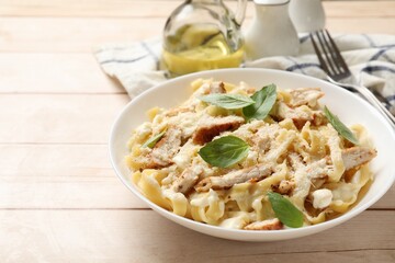 Tasty Alfredo pasta with chicken on light wooden table, space for text