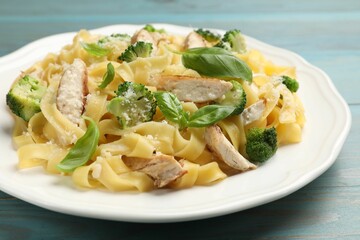 Delicious pasta Alfredo with chicken, cheese, broccoli and basil on light blue wooden table, closeup