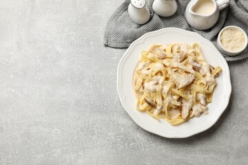 Tasty Alfredo pasta with chicken, cheese and creamy sauce on gray textured table, flat lay. Space for text