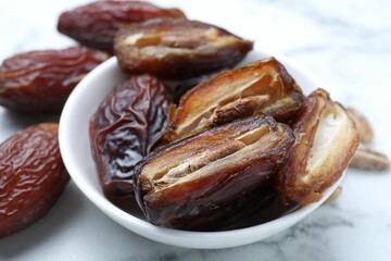 Many tasty dried dates in bowl on light table, closeup
