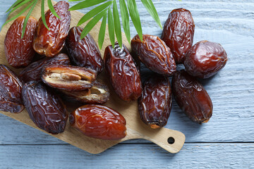 Many tasty dried dates and leaves on blue wooden table, top view