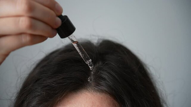 A brunette woman applies a serum for hair and scalp care