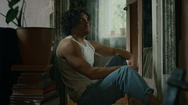 Side tilt shot of tired male writer in undershirt and jeans throwing notebook and pen on floor, going through creative crisis and questioning meaning of his life
