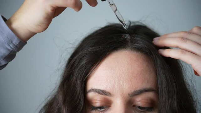 A brunette woman applies a serum for hair and scalp care
