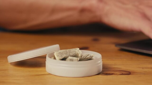 Snus nicotine tobacco close up, pack of tobacco for gum. unhealthy addiction. Man opening box with snus and taking one. 