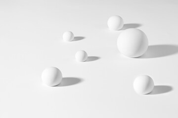 Minimalist composition of white spherical objects on a clean white background with soft shadows...