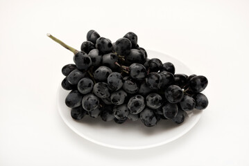 A branch of black grapes on a white plate.