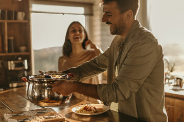 Couple cooking together in a bright kitchen, smiling as they prepare fresh pasta with sunlight streaming in