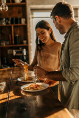Cheerful scene of a couple sharing pasta at their sunny kitchen table