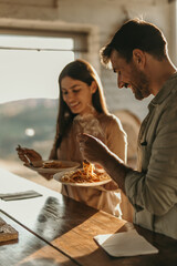 Joyful couple sharing a pasta meal in their sunny kitchen with natural light streaming in