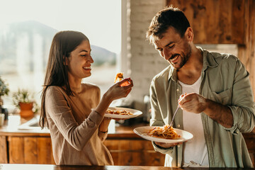 Couple enjoying a cozy pasta lunch together in a bright, sunlit kitchen.