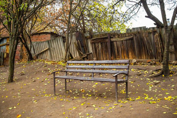 Wooden bench in an old yard with an old wooden fence and trees