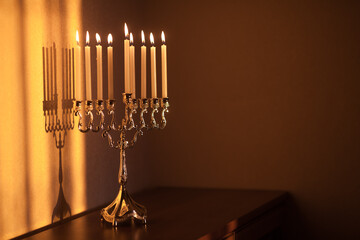 Hanukkah menorah, or hanukkiah in the light of the sun at sunset for Jewish holiday Hanukkah. Hanukkah lamp, nine-branched candelabrum with burning candles with a shadow on the wall.