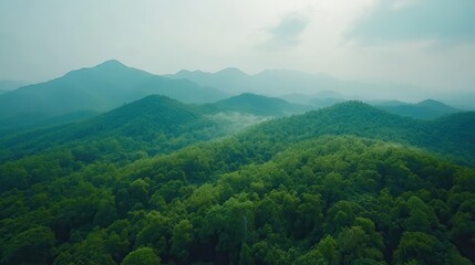 Obraz premium Aerial View of Lush Green Mountains Under Soft Misty Sky with Layers of Forest and Tranquil Landscape Showcasing Nature's Beauty and Serenity in the Wilderness