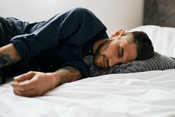 Young bearded man fell asleep on the bed with clothes on. The guy is tired. Daytime sleep at home...