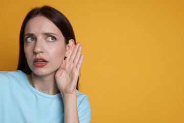 Woman showing hand to ear gesture on orange background, space for text