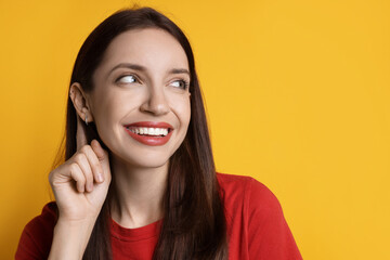 Woman showing hand to ear gesture on orange background. Space for text