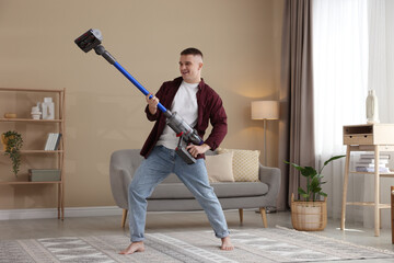 Young man having fun while cleaning rug with cordless vacuum cleaner at home