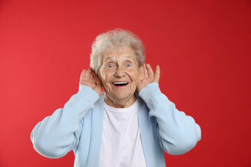 Senior woman showing hand to ear gesture on red background