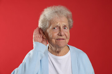 Senior woman showing hand to ear gesture on red background