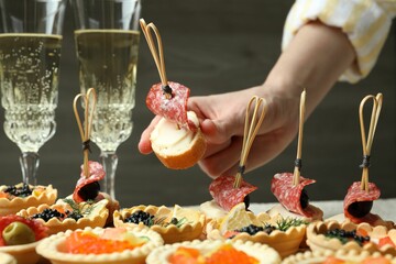 Woman taking tasty canape at table, closeup
