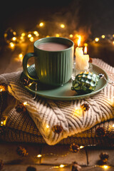 Christmas still life with mug of hot chocolate, candles and christmas lights on stack of knitted sweaters, creating cozy and festive atmosphere for christmas and new year celebrations, greeting card