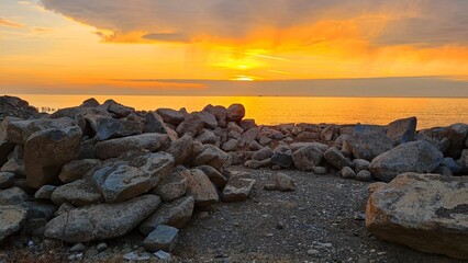 Rocky seashore, golden sun setting into the sea