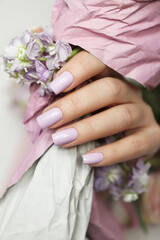 The beautiful hands of a manicured woman hold a bouquet of flowers in close-up.