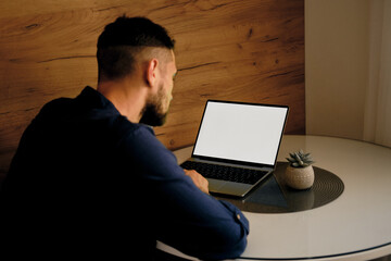 White mock up image blank screen laptop with copy space background for advertising text. Young freelancer man using laptop on kitchen table at home. Marketing and creative design concept.