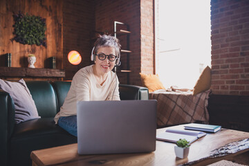 Mature woman enjoying a leisurely weekend at home, seated indoors with cozy decor, using a laptop...