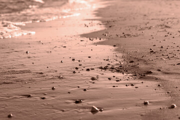 Sea wave on sandy beach with pebbles. Cozy evening abstract background. Demonstrating the colors of 2025 - Mocha Mousse.