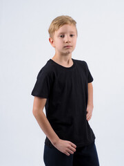 Pleased blonde haired boy points at blank black t shirt shows place for your advertisement focused down isolated over white background. People clothing and promotion concept.