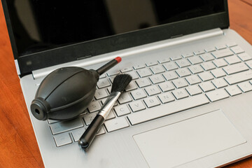 Laptop on wooden table with air pressure cleaner and brush for cleaning dust, Cleanliness concept.