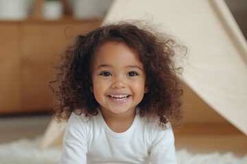 Child with curly hair smiling in a cozy indoor play area near a tent