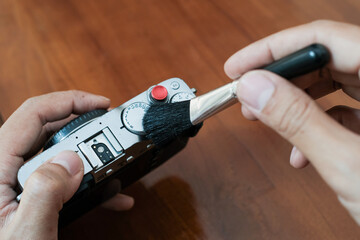 Fototapeta premium Cleaning the camera body with cleaning brush from dust and dirt on wooden table and. Cleaning and care of the camera body. The concept of care for professional photographic equipment.