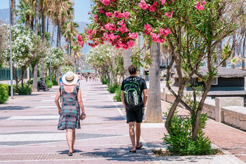 Tourists walking on a seaside promenade with blooming oleander trees. PUERTO BANUS, MARBELLA