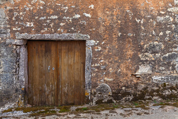 A weathered wooden door set into a rustic stone wall, showcasing the passage of time and the beauty of natural decay