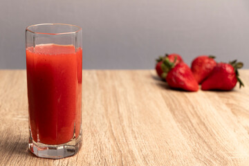 jugo de color rojo en un vaso largo, al fondo fresas desenfocadas