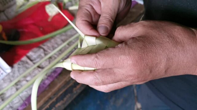 A man weaving young palm fronds, or 'Janur' in Bahasa Indonesia, into Ketupat pouch to be sold.