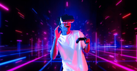 Fototapeta premium Teenager holding joystick and wearing VR goggles while enjoy playing games at neon abstract background. African man enjoy controlling controller and using augmented reality technology. Ingenuity.