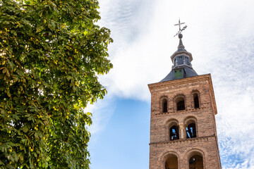 Naklejka premium Iglesia de San Martin (Church of San Martin) Romanesque - Mudejar style bell tower with brick arches on stone columns and weather vane, lush green leaves around, Segovia, Spain.