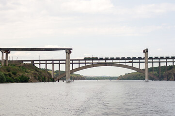 An unfinished bridge spanning a river, with a train traveling on the completed section, highlighting infrastructure development