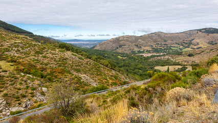 Fototapeta premium Sierra de Gredos mountain landscape with winding tarmac road AV-931 to Plataforma de Gredos parking, Navacepeda de Tormes village in the background, Spain.