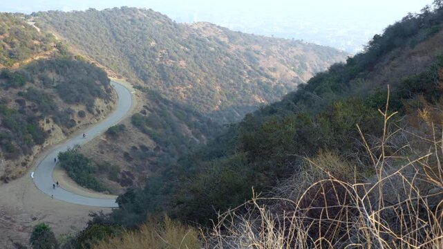 Panoramic view showcasing hazy hills and winding trails in Runyon Canyon Park with people walking against the backdrop of Los Angeles.