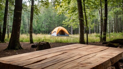 A empty wooden table in the foreground with a tent and trees in the blurred background, suggesting an outdoor camping scene in a forest