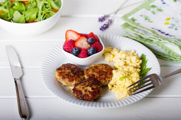 Turkey burgers with scrambled eggs and berries on white wooden background